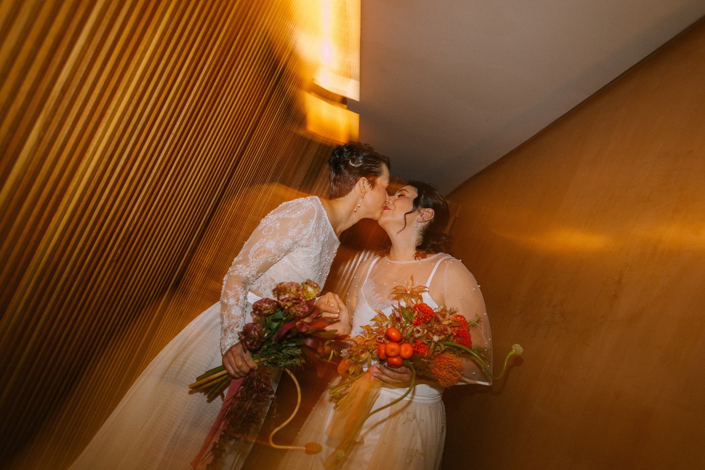 Dani e Karol se beijando no dia do casamento, segurando buquês